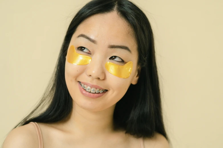 a woman with a yellow eye patch on her face, trending on pexels, mingei, gold body, young asian woman, manuka, smiling slightly