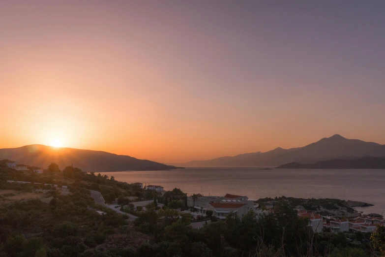 a large body of water next to a lush green hillside, by Exekias, pexels contest winner, romanticism, sunset panorama, distant mountains lights photo, boka, today\'s featured photograph 4k