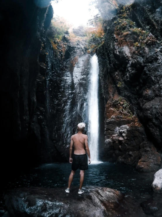 a man standing in front of a waterfall, by Kyle Lambert, pexels contest winner, sumatraism, slightly tanned, full growth from the back, grotto, instagram story