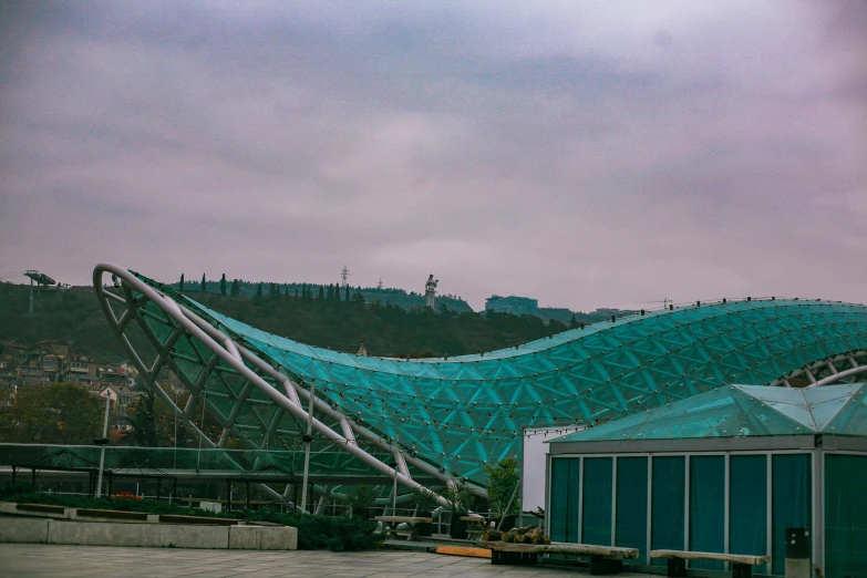 a building with a blue roof and a mountain in the background, inspired by Zha Shibiao, pexels contest winner, stadium, cyan and green, slight overcast weather, square