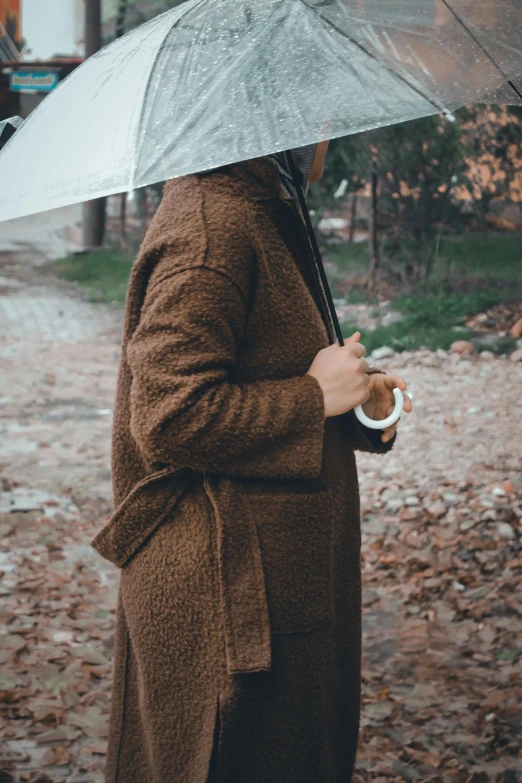 a woman standing in the rain holding an umbrella, trending on unsplash, he is wearing a brown sweater, sustainable materials, next to a tree, fuzzy details