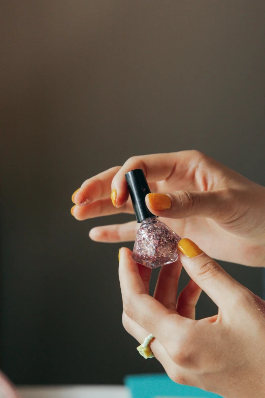 a woman holding a bottle of nail polish, trending on pexels, glitter accents on figure, synthetic bio skin, pink and orange, commercial