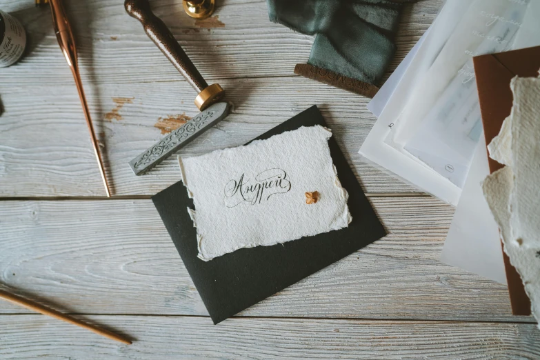 a piece of paper sitting on top of a wooden table, inspired by Avgust Černigoj, pexels contest winner, shop window for magical weapons, gilding, uppercase letter, greeting card