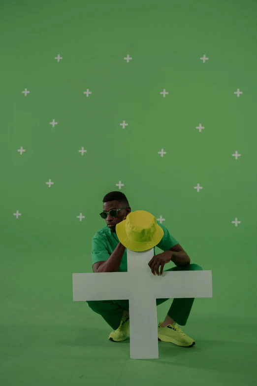 a man sitting on top of a white cross, an album cover, inspired by Paul Georges, trending on pexels, green hat, mkbhd, green and yellow, full body shoot