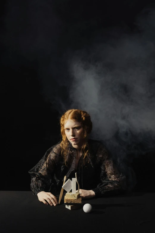 a woman sitting at a table with a ball in front of her, an album cover, inspired by Georges de La Tour, unsplash, renaissance, sullen old maid ( redhead, ghostly smoke, portrait of alexandra daddario, black backdrop