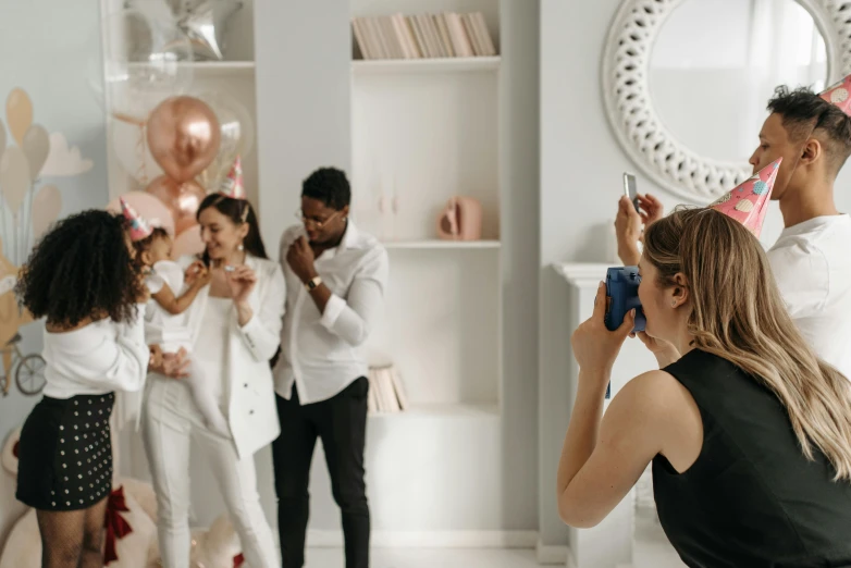 a woman taking a picture of a group of people, pexels contest winner, happening, decoration around the room, photoshoot for skincare brand, families playing, wearing white clothes