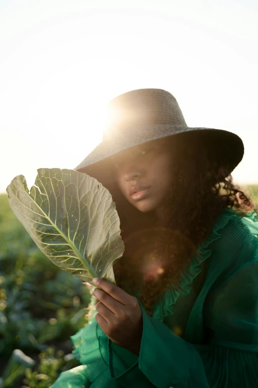 a woman sitting in a field holding a leafy plant, unsplash, renaissance, with afro, standing under a beam of light, farmer, wearing wide sunhat