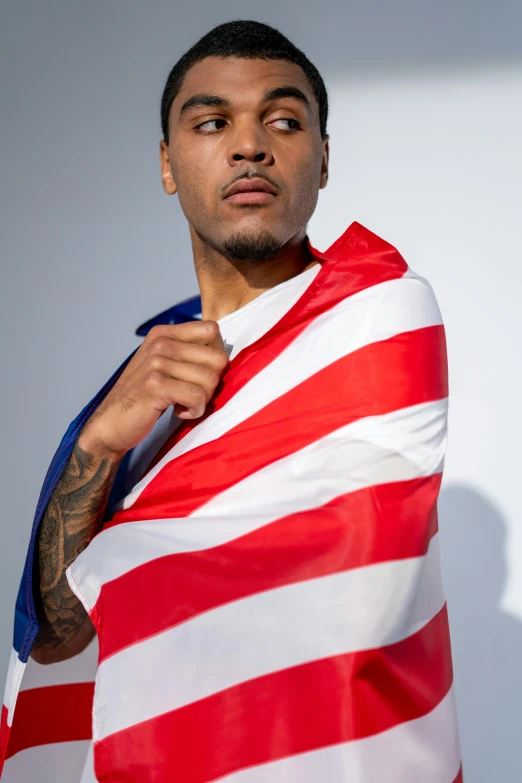 a man is wrapped in an american flag, an album cover, inspired by Christopher Williams, trending on pexels, plain background, neymar jr, nipsey hussle, model pose