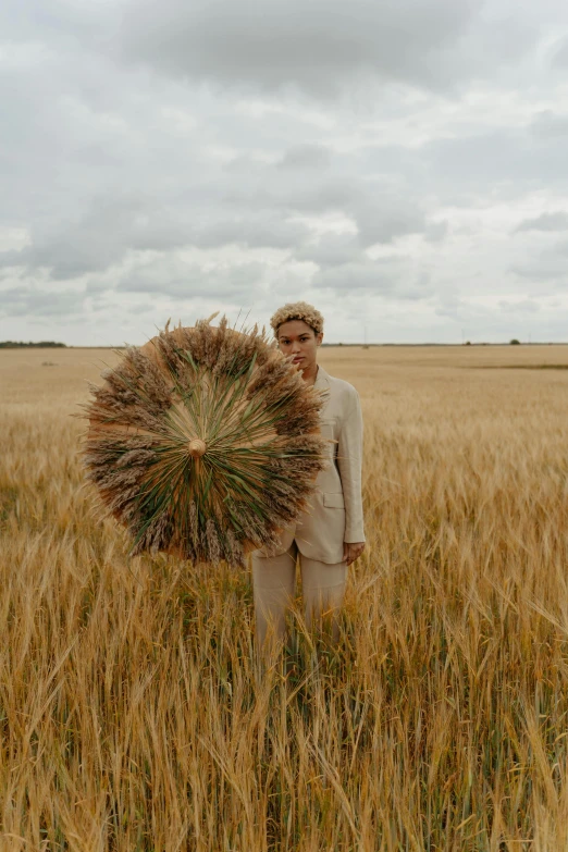 a man standing in a field holding a bunch of wheat, an album cover, by Attila Meszlenyi, unsplash, land art, an oversized beret, ignant, cai xukun, russian clothes