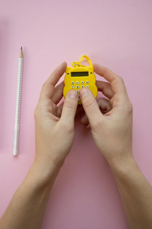 a person using a calculator on a pink surface, yellow magic theme, miniaturecore, hanging, tamagotchi
