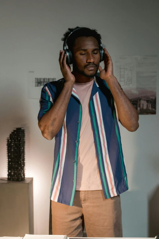 a man holding a pair of headphones to his ear, an album cover, inspired by Paul Georges, trending on pexels, wearing stripe shirt, museum photoshot, frank ocean, low light cinematic