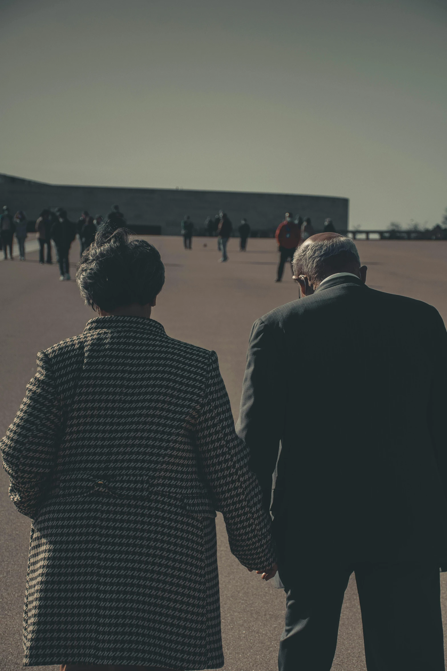 a man and a woman holding hands in a parking lot, unsplash, visual art, walk in a funeral procession, ( ( theatrical ) ), elderly, low sun