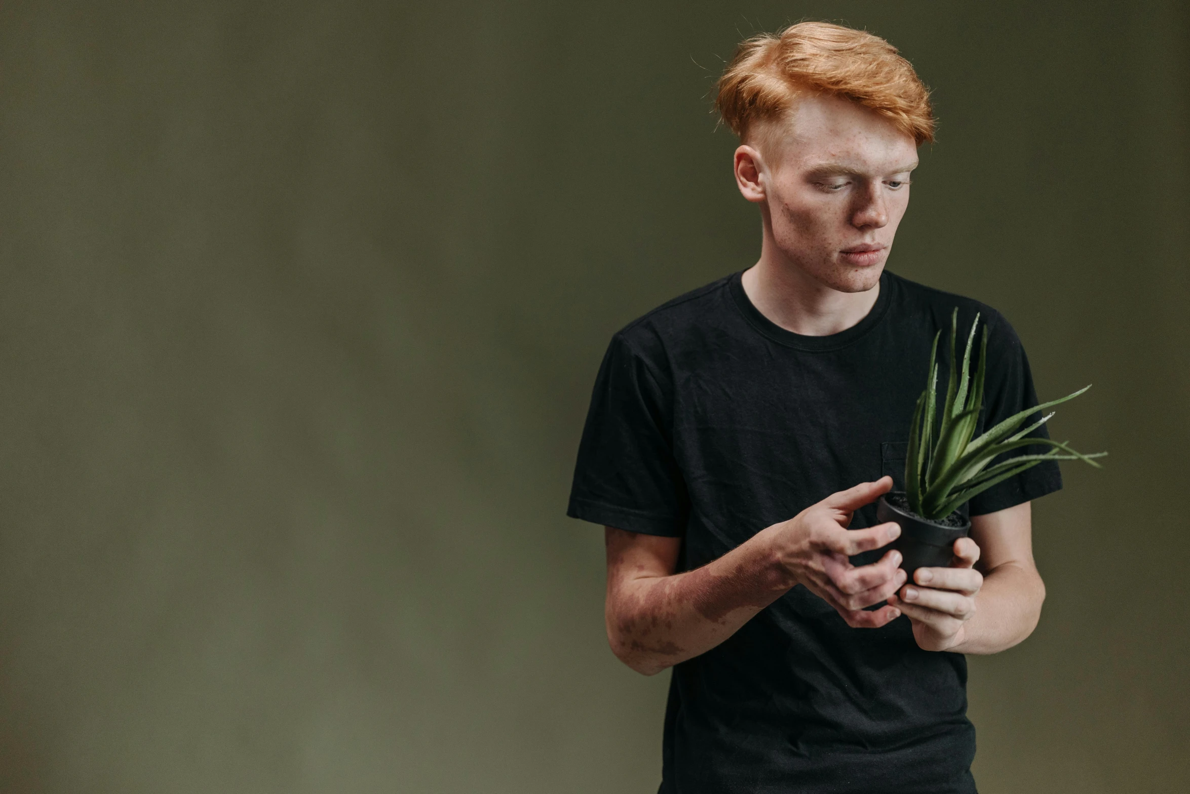 a man in a black shirt holding a potted plant, pexels contest winner, red haired teen boy, ignant, pale and sickly, product introduction photo