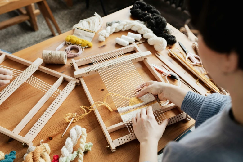 a woman sitting at a table working on a weaving loom, trending on pexels, arts and crafts movement, with a bunch of stuff, a wooden, knolling, thumbnail