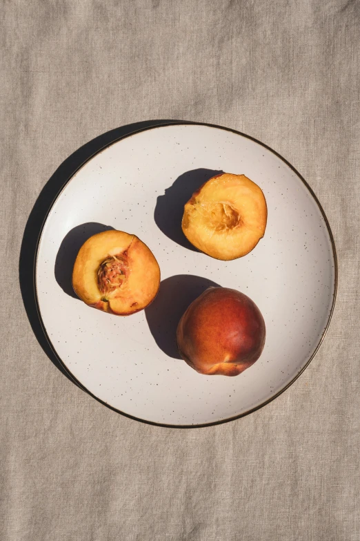 a white plate topped with three pieces of fruit, unsplash, photorealism, peach, linen, full frame image, seasonal