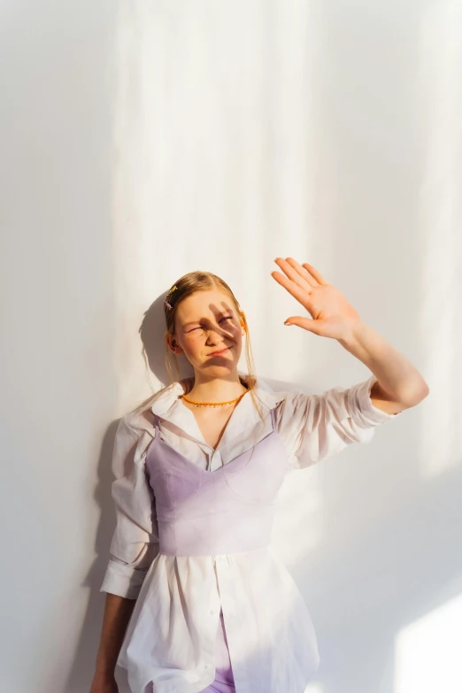 a woman standing in front of a white wall, an album cover, inspired by Anna Füssli, unsplash, renaissance, crying and reaching with her arm, betty cooper, sunlight, purple eyes and white dress