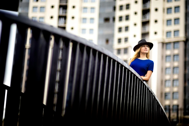 a woman in a hat standing on a bridge, a portrait, by Niko Henrichon, art photography, square, in sao paulo, blue and black, shot on sony alpha dslr-a300