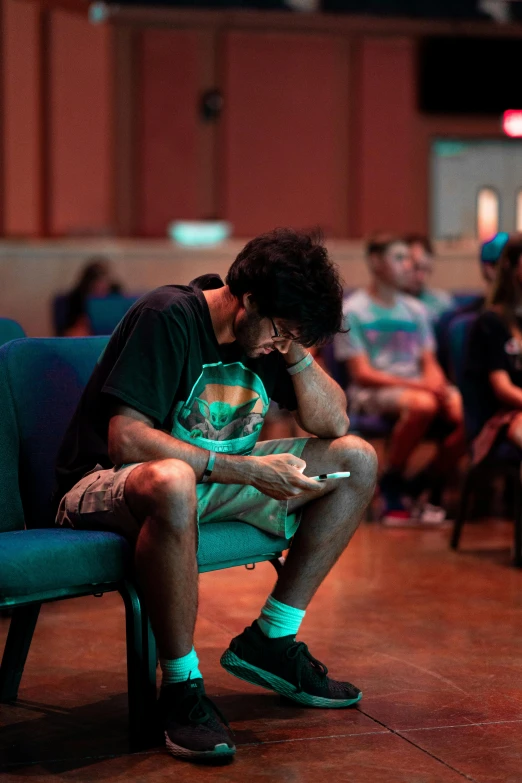 a man sitting in a chair looking at his cell phone, by Scott Gustafson, pexels, happening, scene from church, looking exhausted, at college, people enjoying the show