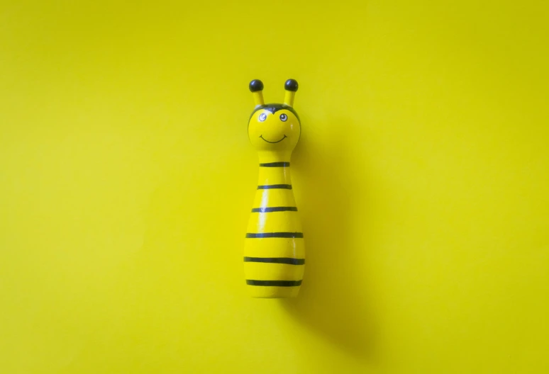 a close up of a toy giraffe on a yellow background, by Andries Stock, pexels contest winner, minimalism, a hookah smoking caterpillar, cute funny figurine wooden, stripes, bee