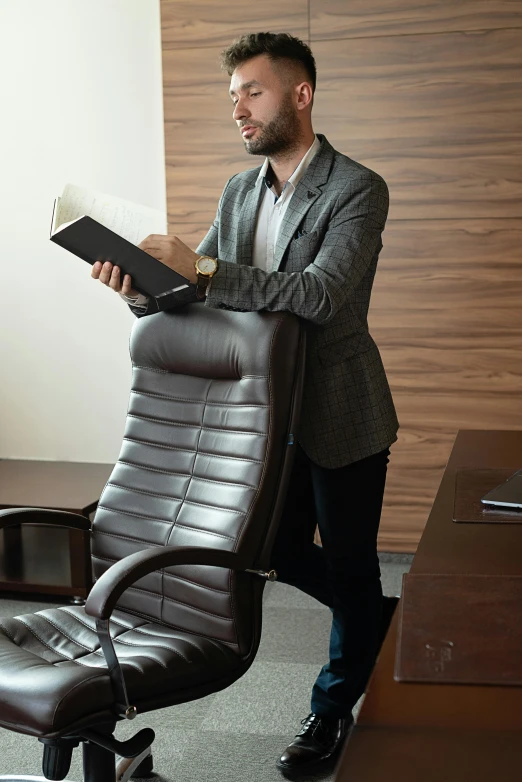 a man reading a book in an office chair, standing elegantly, brown