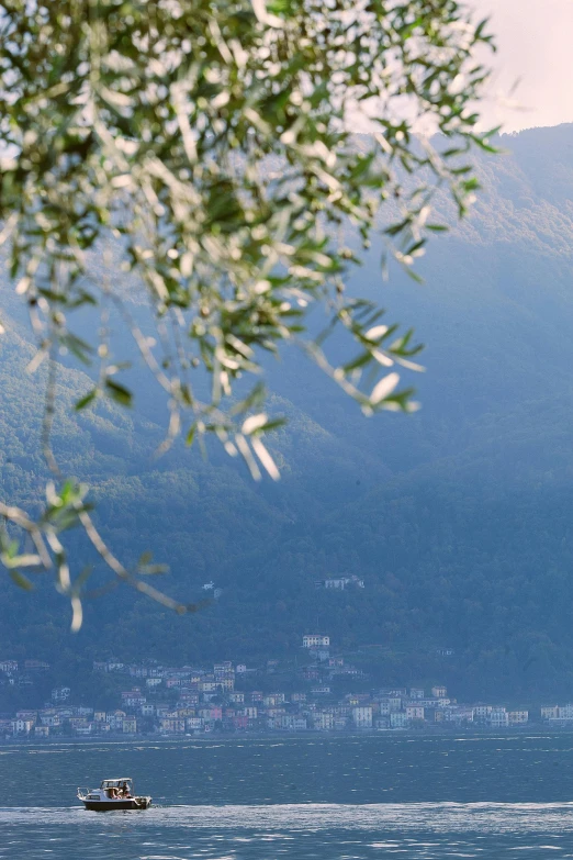 a large body of water with a boat in it, a picture, inspired by Serafino De Tivoli, trending on unsplash, arabesque, distant town in valley and hills, overhanging branches, slim aarons, overview