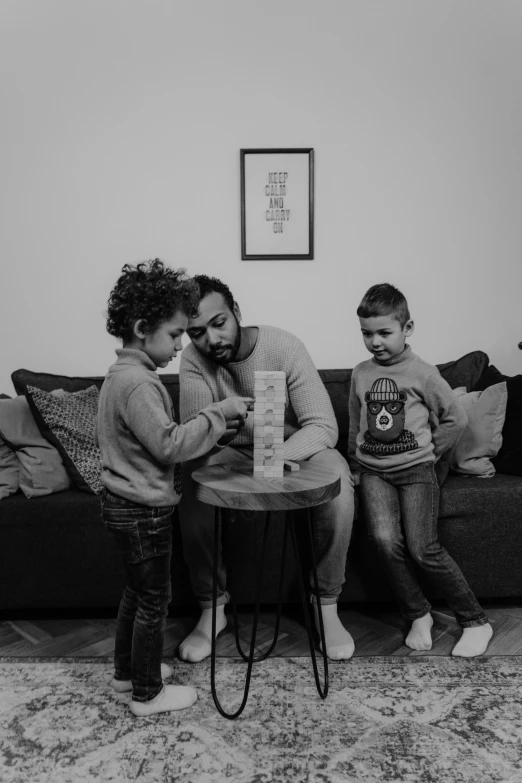 a man and two children sitting on a couch, a black and white photo, by Ahmed Yacoubi, pexels contest winner, les nabis, board games, cardistry, 2 years old, on a canva