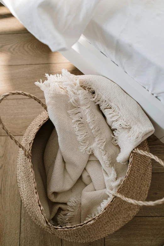 a basket sitting on top of a wooden floor next to a bed, by Nina Hamnett, unsplash, baroque, ecru cloth, towels, detailed product shot, light tan