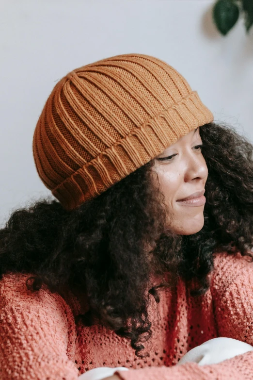 a woman sitting at a table with a cup of coffee, wearing beanie, orange hue, with textured hair and skin, thumbnail