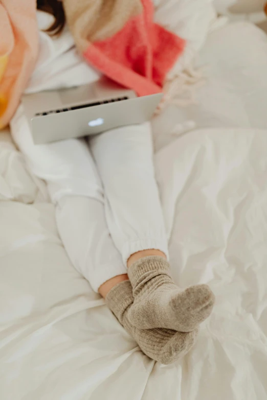 a woman sitting on a bed with a laptop, by Carey Morris, trending on pexels, white leggings, browns and whites, bottom angle, seasonal