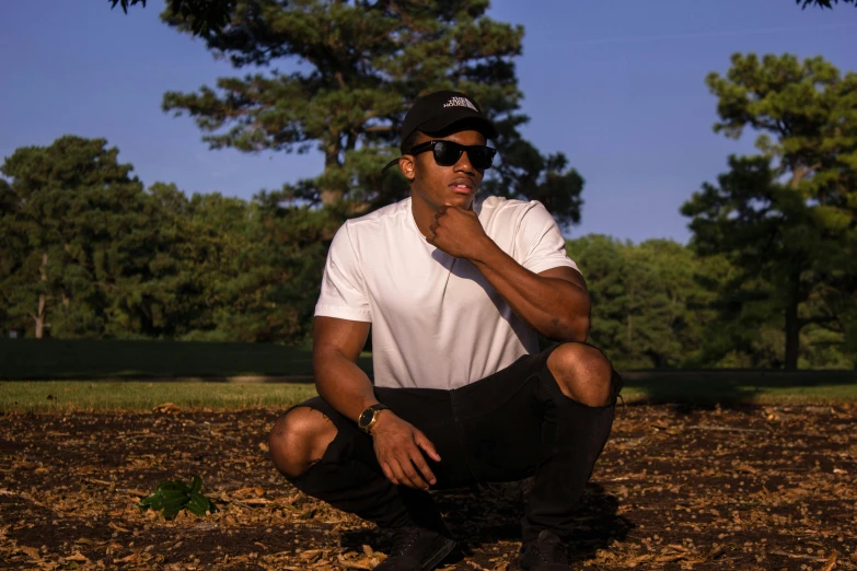 a man sitting on the ground in a park, memphis rap, profile image, shades, man standing in defensive pose