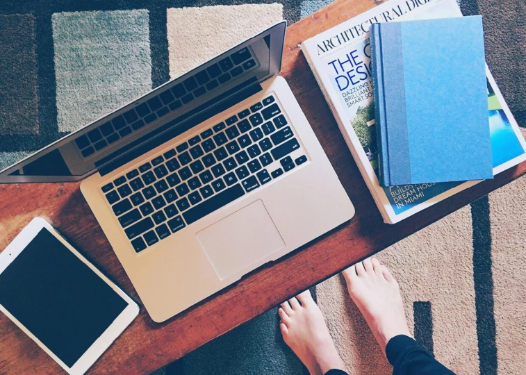 a laptop computer sitting on top of a wooden table, by Carey Morris, unsplash, feet on the ground, 9 9 designs, wooden desks with books, sitting in french apartment