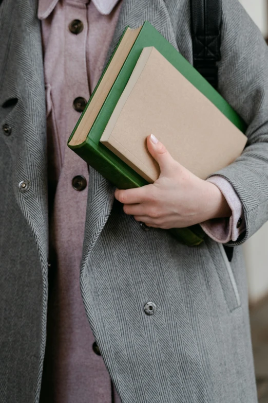 a close up of a person holding a book, by Helen Stevenson, wearing hunter coat, sustainable materials, wearing a blazer, sage green