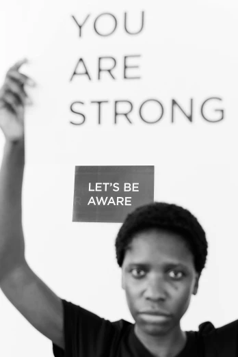a man holding up a sign that says you are strong, a black and white photo, inspired by Carrie Mae Weems, pexels contest winner, black arts movement, african woman, emergency, marina abramovic, let there be light