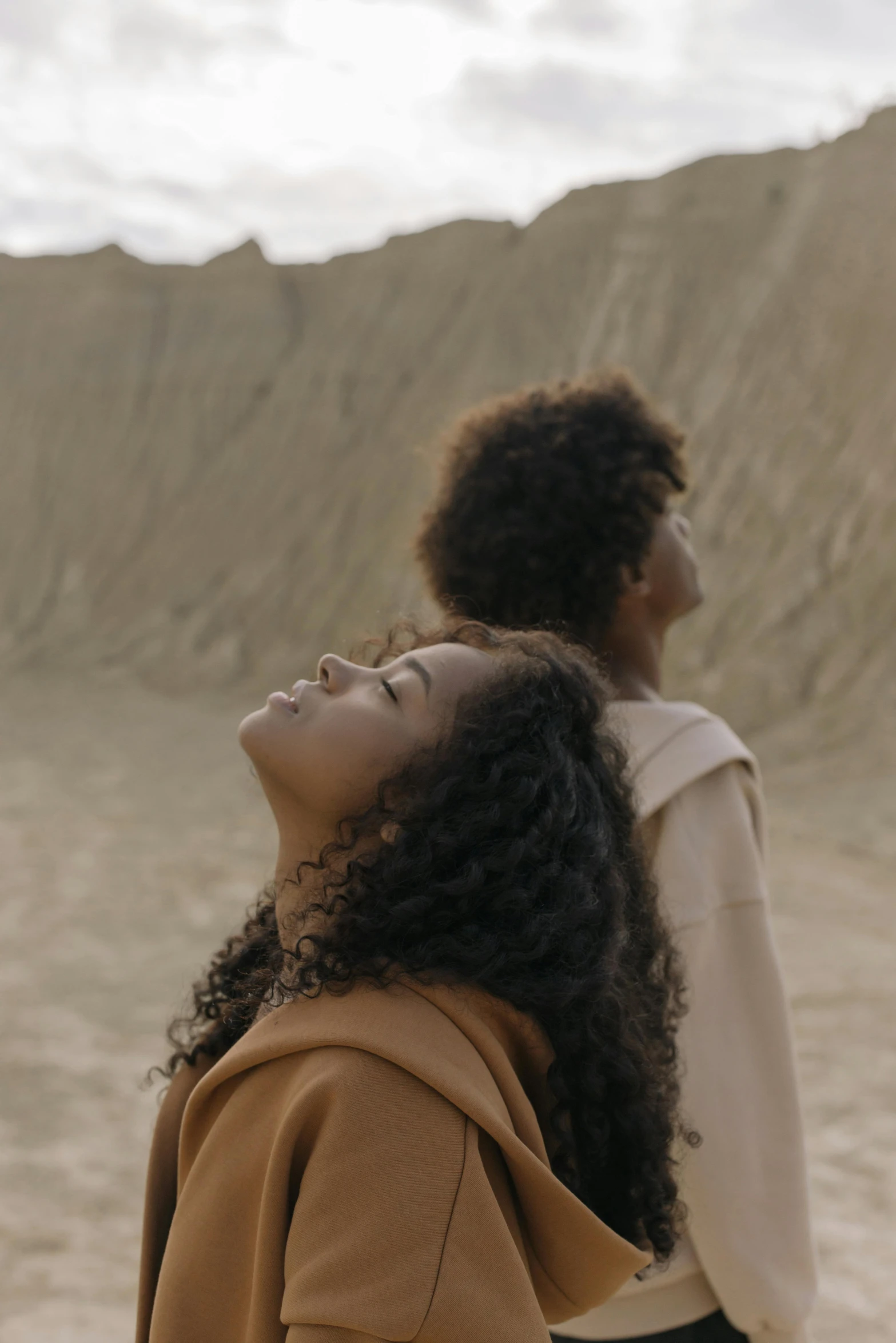 a couple of women standing next to each other, trending on unsplash, afrofuturism, falling sand inside, still frame from a movie, young woman looking up, heavenly