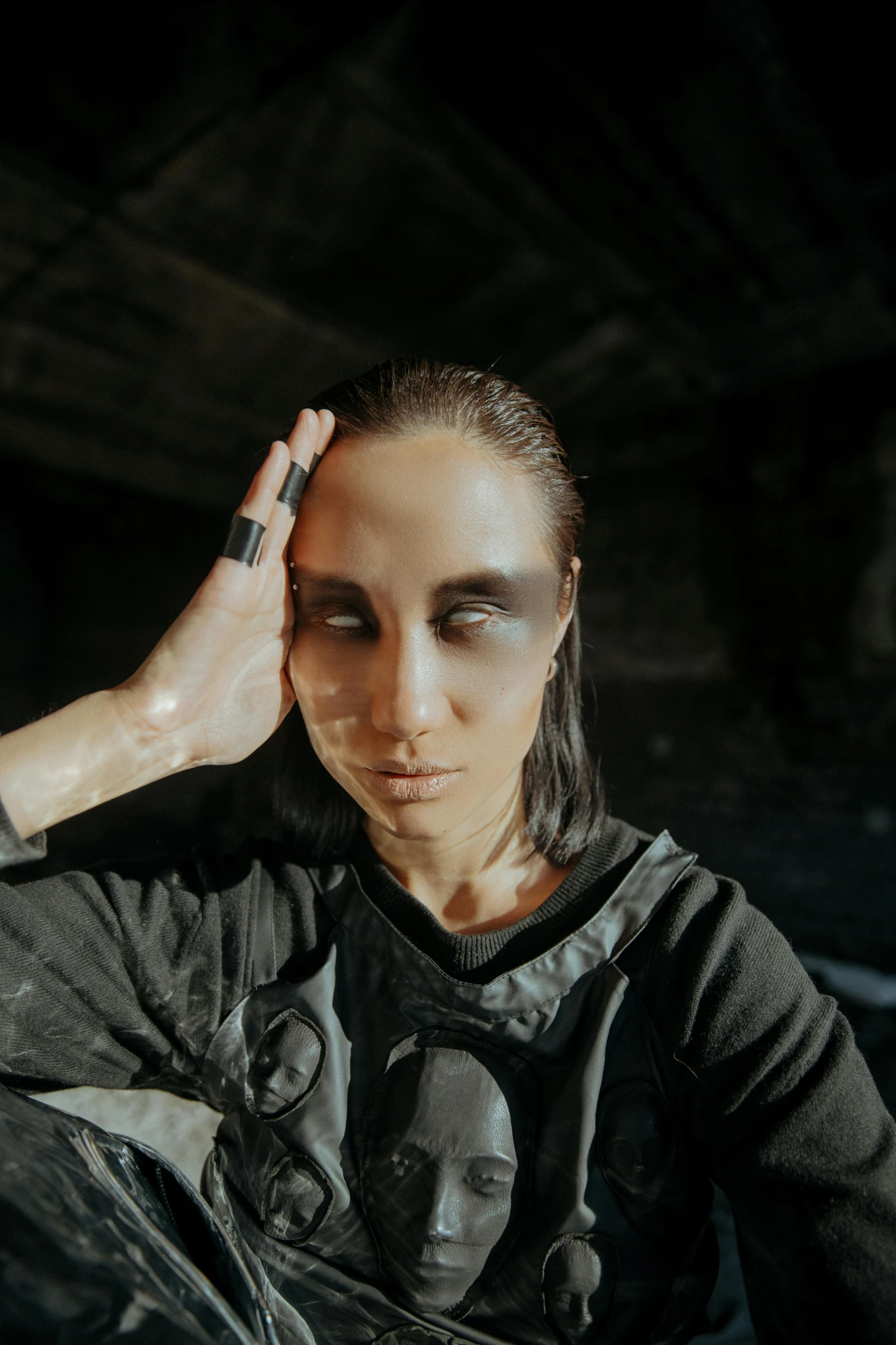 a woman sitting in a chair with her hand on her head, an album cover, inspired by Anna Füssli, antipodeans, wearing techwear and armor, black eye shadow, 2019 trending photo, synthetic bio skin