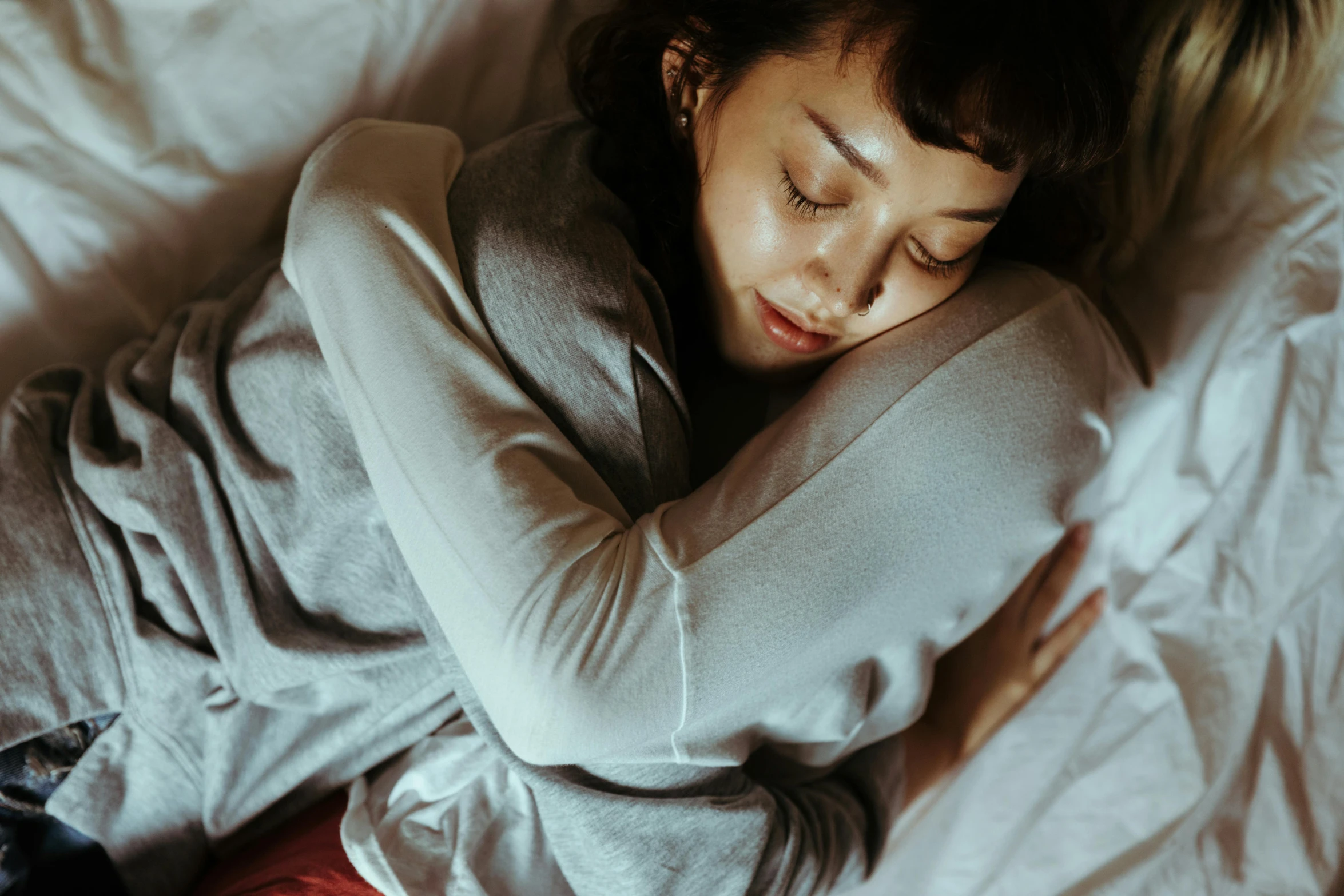 a woman laying on top of a bed next to a cat, inspired by Elsa Bleda, trending on pexels, romanticism, wearing a grey robe, kiko mizuhara, hugging each other, crossed arms