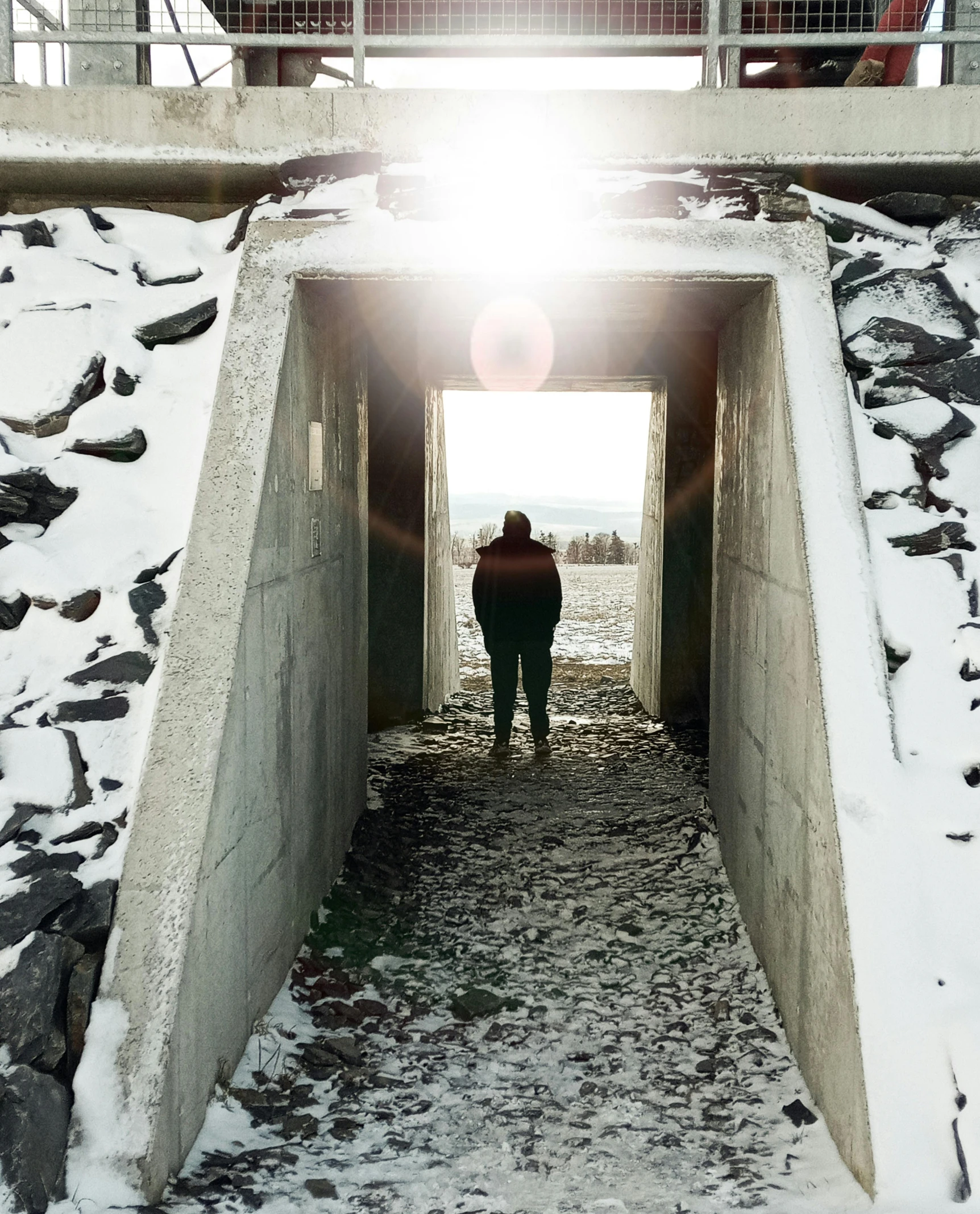 a person walking through a tunnel in the snow, an album cover, pexels contest winner, giant tomb structures, harsh overhead sunlight, looking at the ground, bunker