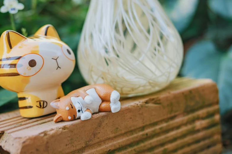 a cat figurine sitting on top of a wooden block, a cartoon, by Julia Pishtar, unsplash, wind chimes, lying down, shiba figurine, sitting in the garden