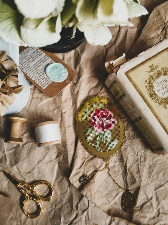 a book sitting on top of a table next to a vase of flowers, a cross stitch, inspired by Eden Box, pexels contest winner, arts and crafts movement, vintage makeup, jovana rikalo, aerial view. hand stitching, gilded. floral