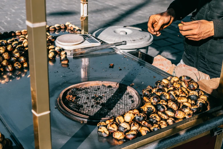 a man standing next to a grill filled with lots of food, by Julia Pishtar, trending on unsplash, hurufiyya, snails, street vendors, on a sunny day, abalone