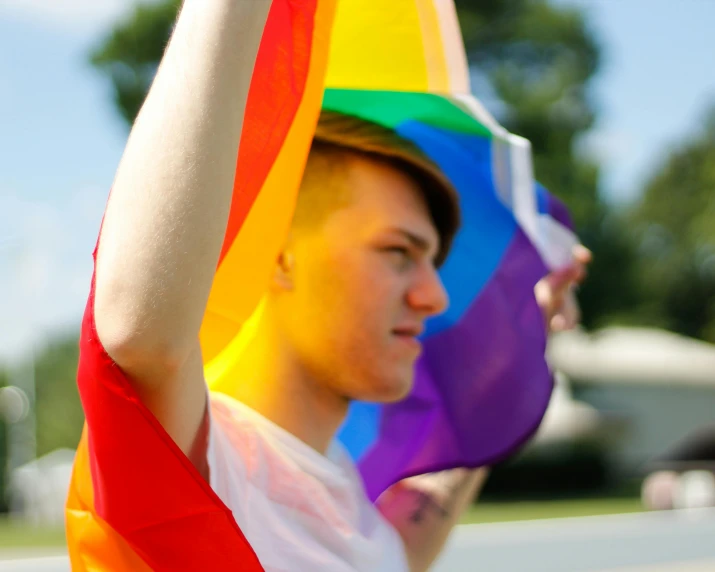 a close up of a person holding a rainbow flag, red haired teen boy, pictured from the shoulders up, waving, profile image