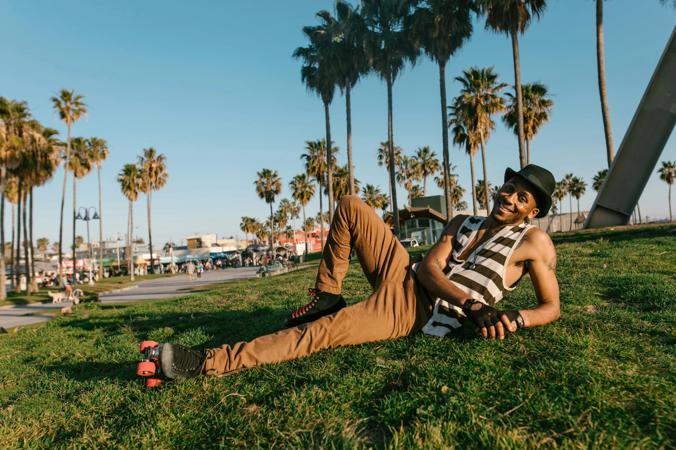a man laying on the grass in front of palm trees, by Julia Pishtar, unsplash, afropunk, santa monica beach, a suited man in a hat, in an urban setting