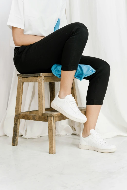 a woman sitting on top of a wooden stool, wearing white sneakers, full product shot, zoomed in, full shot ( fs )