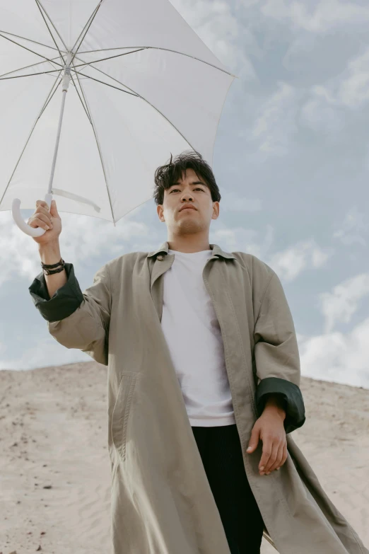 a man in a trench coat holding an umbrella, by Robbie Trevino, half asian, sunny sky, asher duran, low quality photo