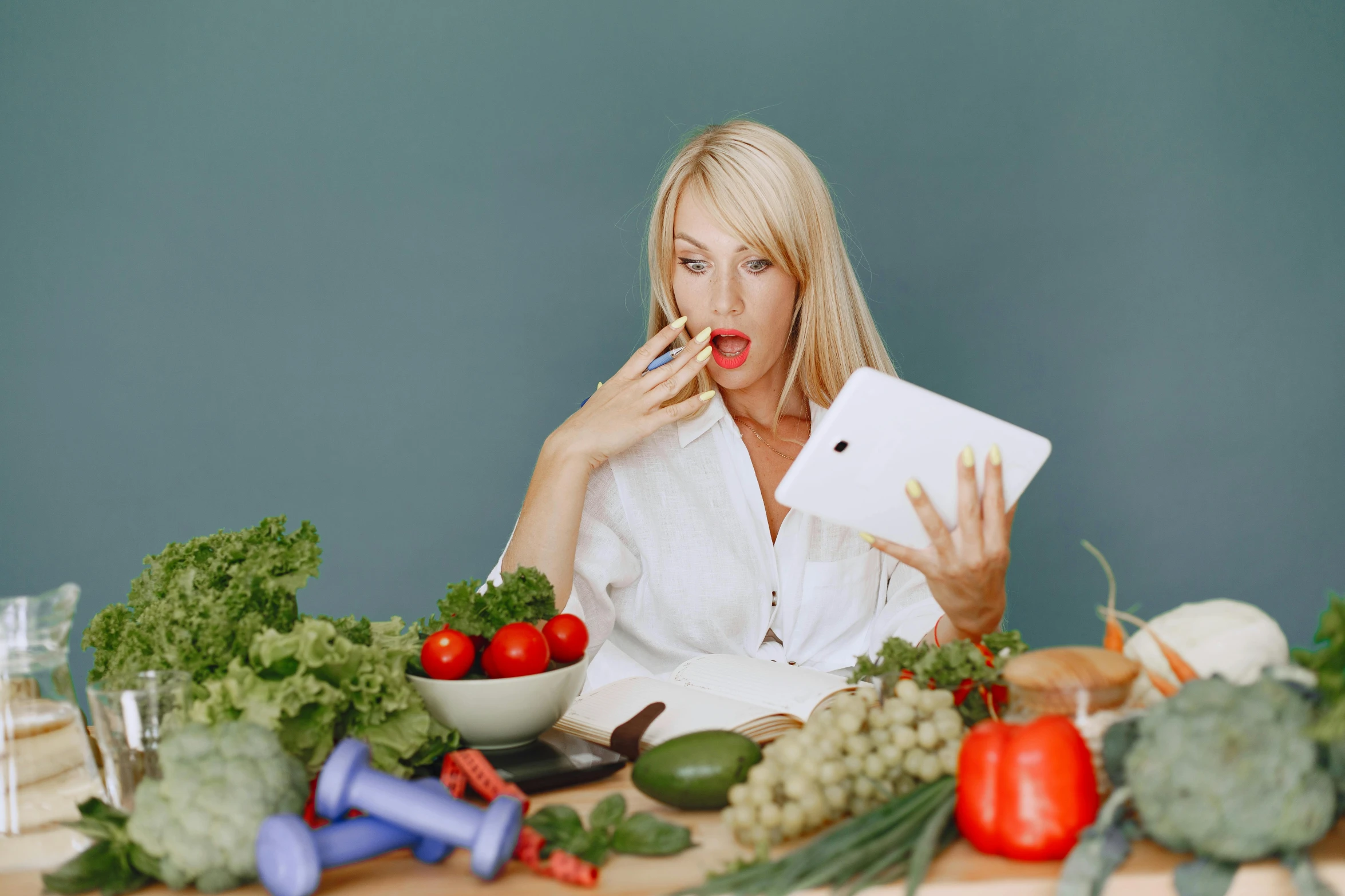 a woman sitting at a table with a tablet in front of her, a picture, by Julia Pishtar, pexels contest winner, vegetables, licking out, very surprised, blonde women