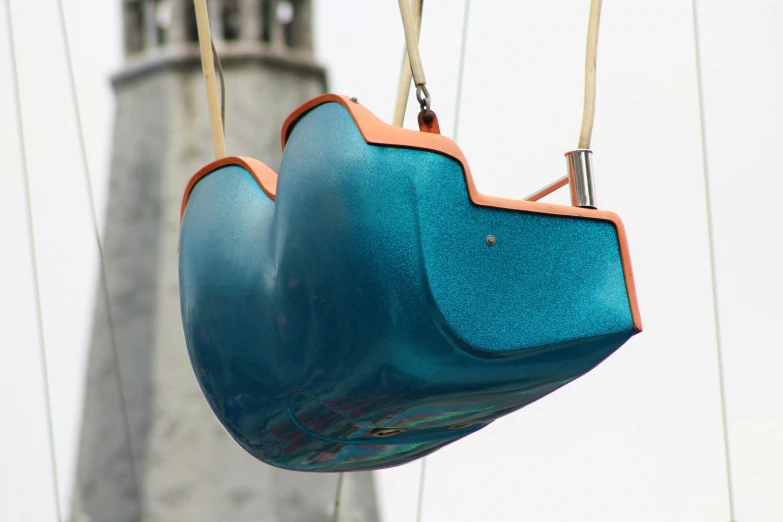 a blue and orange swing with a tower in the background, an abstract sculpture, by Doug Ohlson, unsplash, neck zoomed in from lips down, glass helmets and dove wings, high angle close up shot, teal gradient