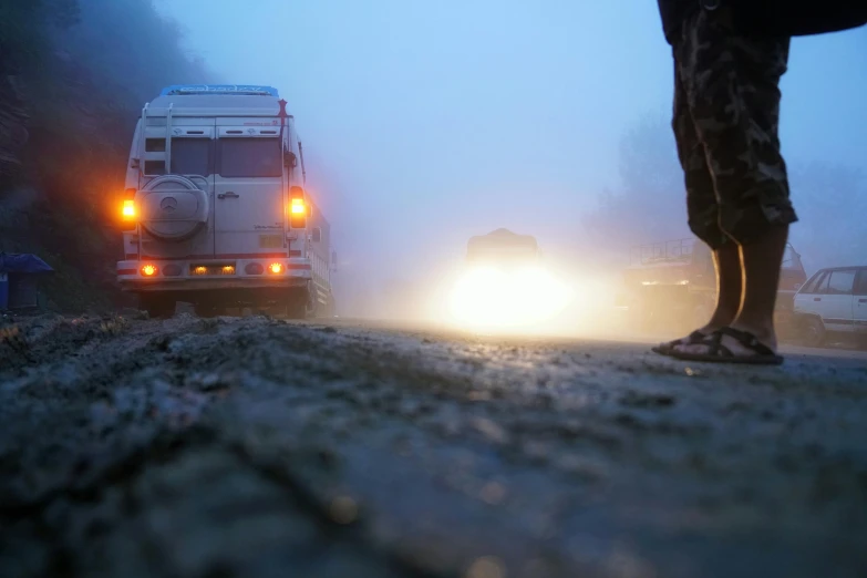 a person standing in front of a van on a foggy road, rocky roads, land rover defender, ukraine, midnight fog - mist!