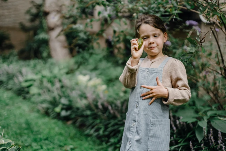 a little girl that is standing in the grass, by Emma Andijewska, pexels contest winner, starving artist wearing overalls, holding a cigar, seeds, standing in a botanical garden