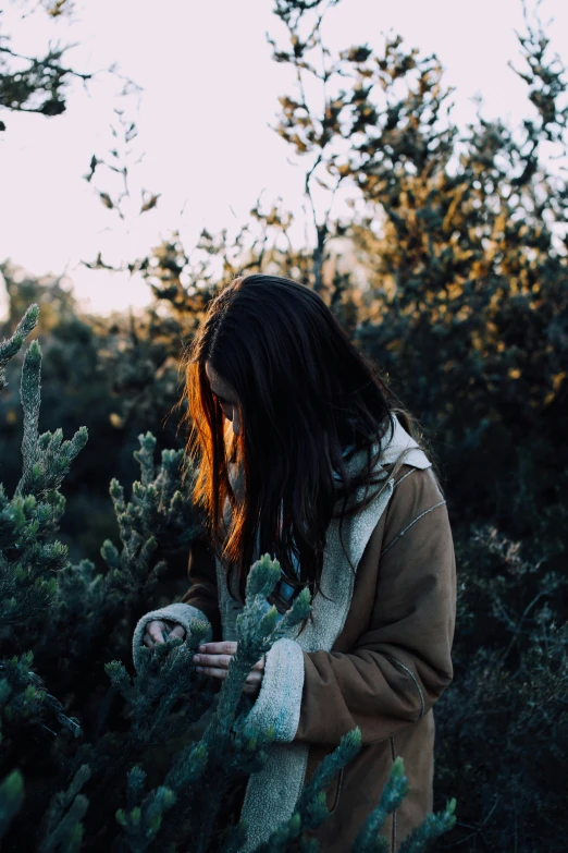 a woman standing in the middle of a forest, inspired by Elsa Bleda, unsplash contest winner, australian tonalism, holding a cactus, black haired girl wearing hoodie, with soft bushes, gardening