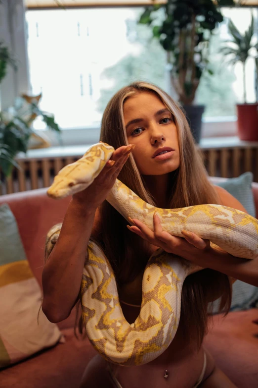 a woman sitting on a couch holding a snake, trending on pexels, 1 8 yo, 2 animals, with long blond hair, brunette